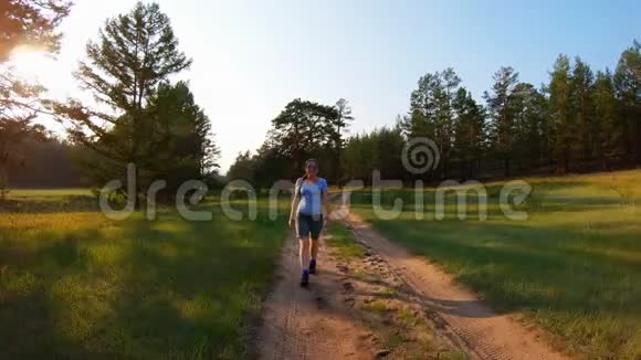 穿着短裤和蓝色眼镜的女孩在日落时走在乡间小路上视频的预览图