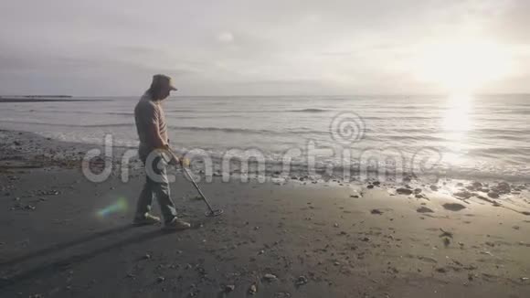 人类正在海滩上遛狗手持探测器在日出时在海岸线上的沙滩上发现金属视频的预览图
