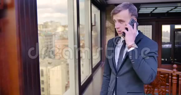 商人的电话交谈一个年轻人穿着灰色西装站在靠近窗户的办公室里打电话视频的预览图