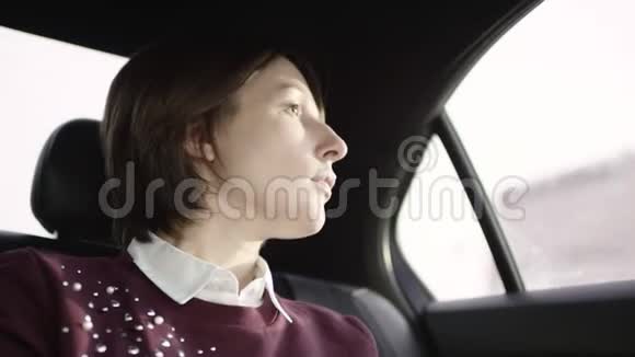 漂亮的女人棕色头发穿着白色衬衫和栗色毛衣坐在车里看着窗户视频的预览图