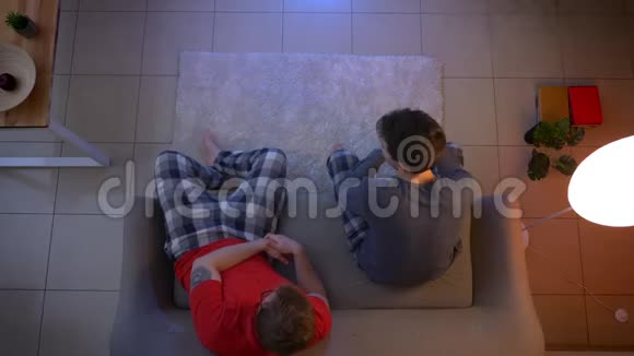 两个穿睡衣的年轻人坐在沙发上在客厅里交流看电视视频的预览图