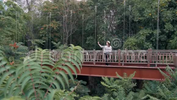 千禧潮女游客使用智能手机在丛林中的桥上自拍视频的预览图