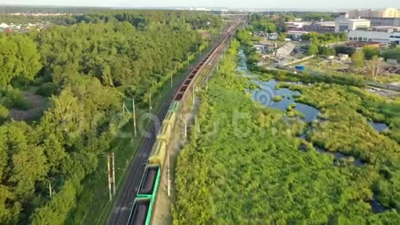 在阳光明媚的夏天一列有建筑材料的火车在田野和森林的背景下乘火车行驶视频的预览图