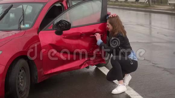 一个受惊的女孩在湿漉漉的路上车祸后在她的破车旁的肖像视频的预览图