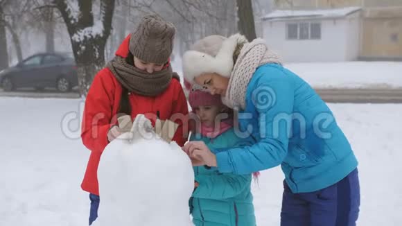 妈妈和两个女儿在冬天装饰鹅卵石一起堆雪人视频的预览图