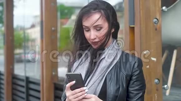年轻的女人拿着电话看着微笑着长发在大风中发展视频的预览图