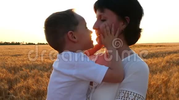 一位快乐的母亲在夕阳的背景下亲吻一个抱着他在麦田里的孩子视频的预览图
