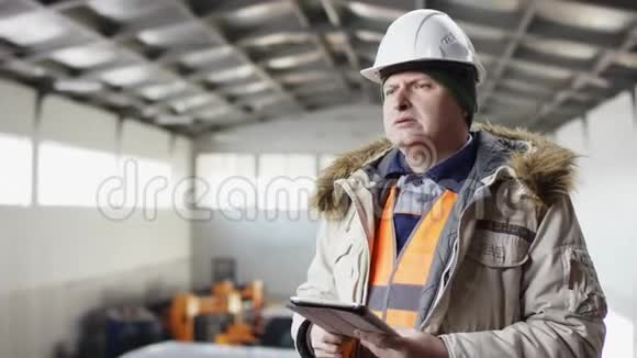 一个戴着安全帽穿着工作服的人正站在机库的中间拿着平板电脑对着镜头偷东西视频的预览图