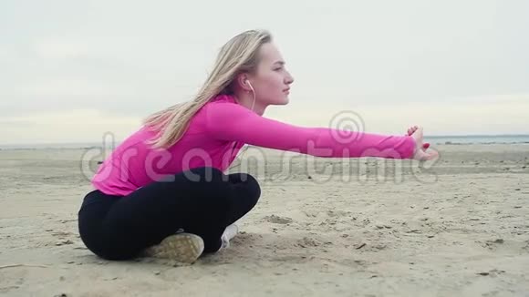 年轻迷人的女孩在空海沙滩上用耳机做瑜伽视频的预览图