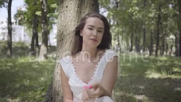 一位年轻貌美的少女长着一头深色长发穿着一件白色的夏装坐在树下视频的预览图