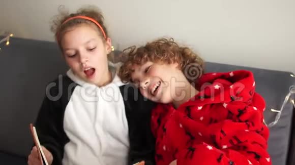 穿着睡衣的哥哥和姐姐在圣诞节假期读一本书圣诞快乐视频的预览图