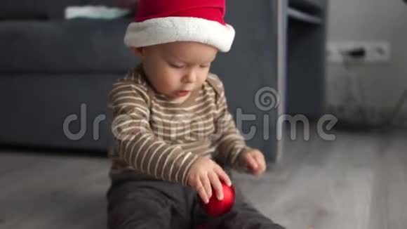 戴圣诞帽的婴儿在室内地板上玩圣诞球新年快乐圣诞快乐视频的预览图