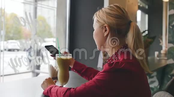 女孩微笑着在咖啡馆里等着见面在她的智能手机上自拍慢动作视频的预览图
