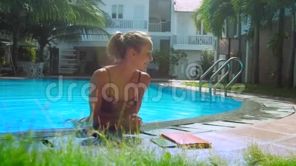 穿比基尼的漂亮金发女孩躺在泳池边微笑视频的预览图