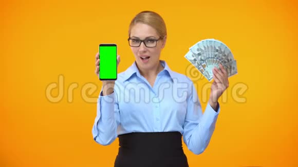 漂亮的白种人女士展示绿色屏幕智能手机和美元现金回来了视频的预览图
