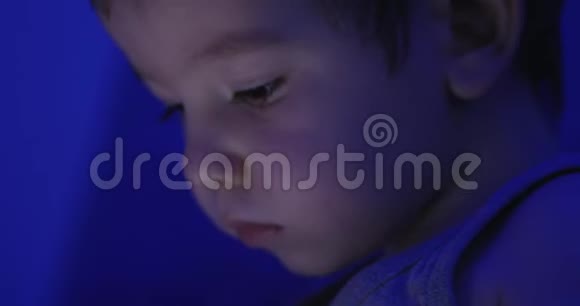 一个可爱的白种人小男孩特写一个孩子的夜景从一台平板电脑上观看视频的预览图