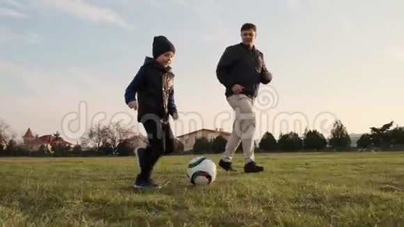 快乐的儿子和爸爸在操场上奔跑一个接一个慢动作踢足球的特写镜头视频的预览图
