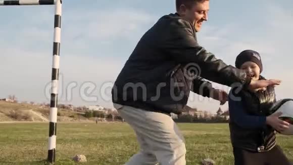 儿子摔倒在草地上和他有趣的爸爸慢动作在足球比赛中大笑视频的预览图