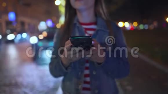 女人在夜城的街道上行走时使用智能手机视频的预览图