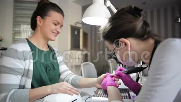 在一家美容院修五金指甲美甲师使用电钉锉钻对女性手指进行美甲视频的预览图