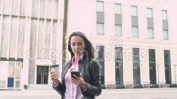 漂亮的商业女孩站在街头背景看着电话喝着一杯纸杯里的咖啡强者视频的预览图