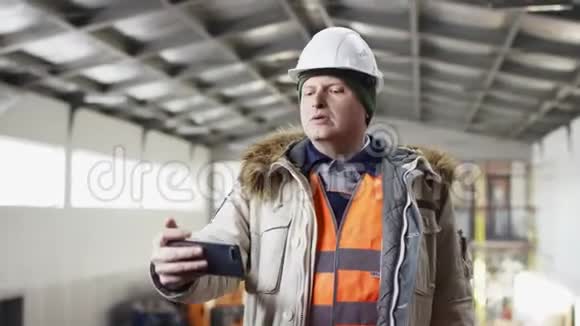 一个戴着安全帽穿着工作服的人正站在机库的中央用手机在机库里拍照视频的预览图