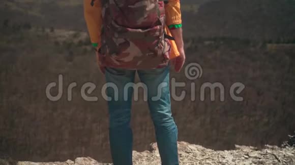 一个穿着黄色夹克眼镜和旅游背包的人站在山上举起双手象征着自由视频的预览图