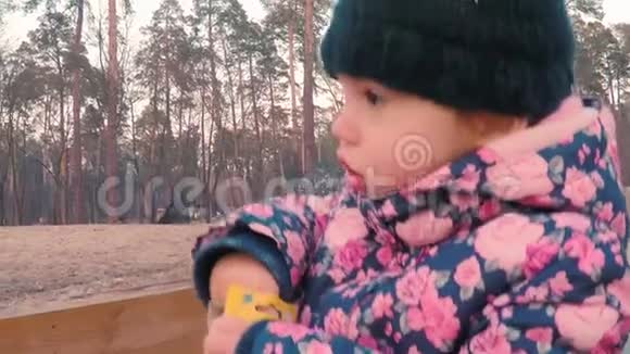 一个穿着五颜六色的粉红色夹克的小可爱女孩从爸爸手里拿白色粉笔在公园的一个儿童游乐场附近视频的预览图