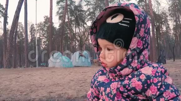 一个穿着五颜六色的粉红色夹克的小可爱女孩正坐在公园里儿童游乐场附近长凳上视频的预览图