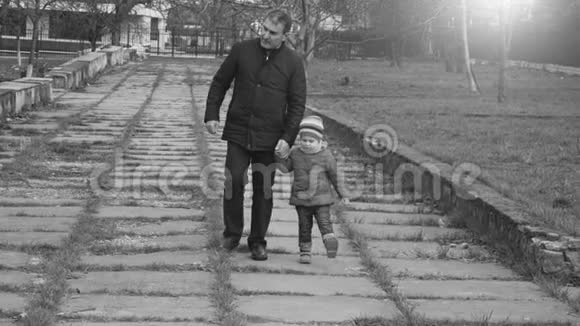 孙女和爷爷牵着手走在城市公园里又黑又白慢动作视频的预览图