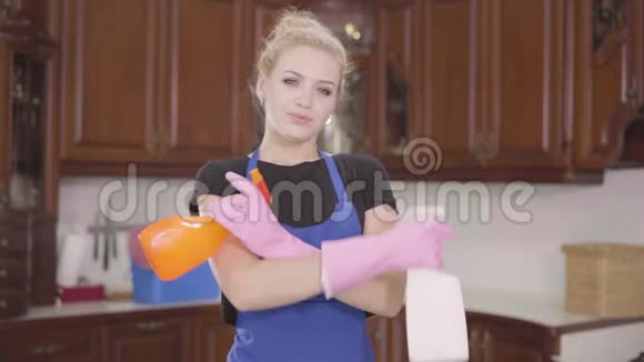 年轻漂亮的女人站在厨房里双手交叉着拿着洗洁精的瓶子看着镜头视频的预览图