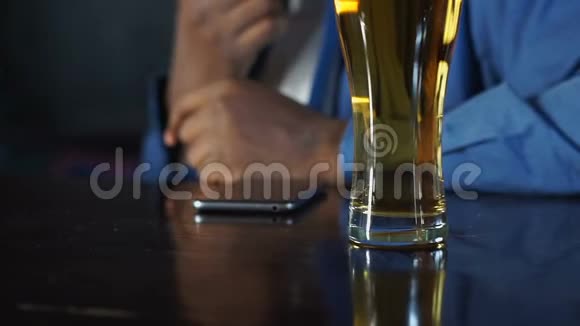 非裔美国人坐在体育酒吧喝啤酒等电话视频的预览图