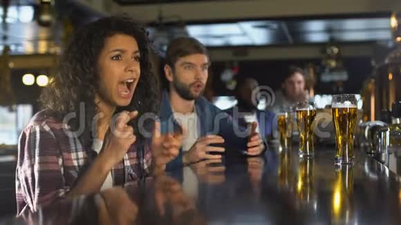双种族女孩和男迷在酒吧里看体育比赛对比分失望视频的预览图