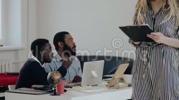 快乐年轻迷人的高加索经理商务女性与两位黑人男性同事在现代办公桌上交谈视频的预览图