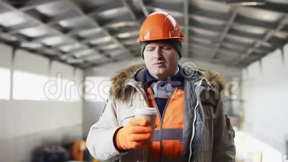 戴着安全帽穿着工作服的人正站在机库的中间对着镜头喝着杯咖啡视频的预览图