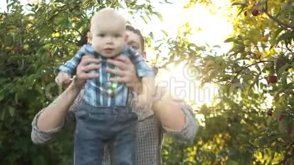 快乐的父亲在花园里肩上搭肩快乐的微笑男孩在肩上爸爸看着镜头视频的预览图