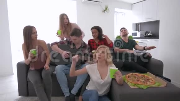 一群多种族的朋友坐在一间现代化的大公寓里的沙发上跳舞唱歌而男孩则扮演着视频的预览图