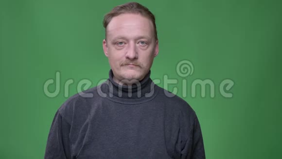 金发中年男子穿灰色套头衫在绿色背景下平静地观看镜头的肖像视频的预览图