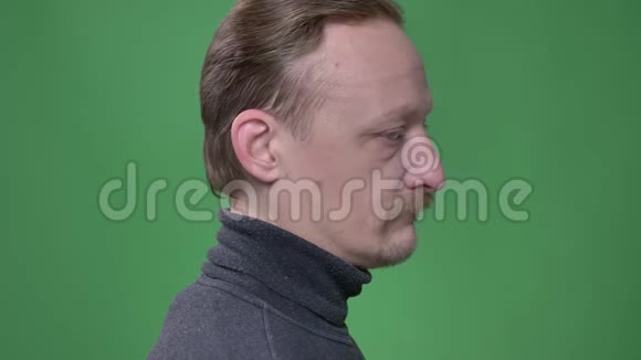 中年严肃男子留胡子的肖像转向相机在绿色背景上冷笑着观看视频的预览图