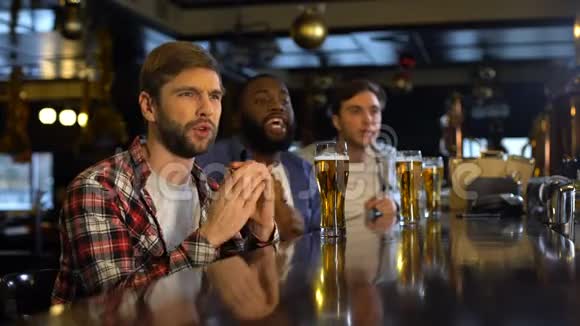 男性朋友喝啤酒为酒吧里的体育比赛加油为输球烦恼视频的预览图