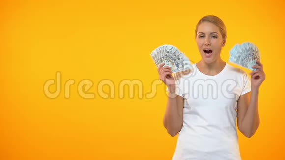 兴奋的女人在橙色背景上显示美元钞票彩票中奖收入视频的预览图