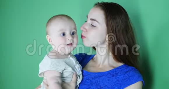 年轻的妈妈穿着蓝色连衣裙亲吻一个可爱的6个月大的婴儿视频的预览图