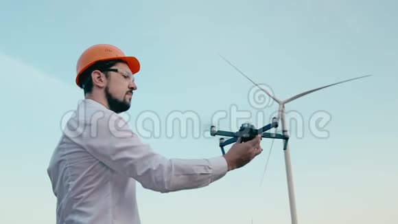 戴着橙色防护头盔和带有遥控器的护目镜的白种人工程师将一架智能四翼飞机无人机举到视频的预览图