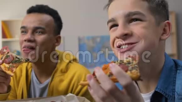 两个朋友笑着在电视上看情景喜剧系列片一边吃披萨视频的预览图