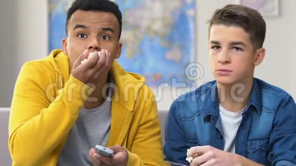 两个邋遢的十几岁男孩在电视上看电影吃爆米花家庭娱乐视频的预览图