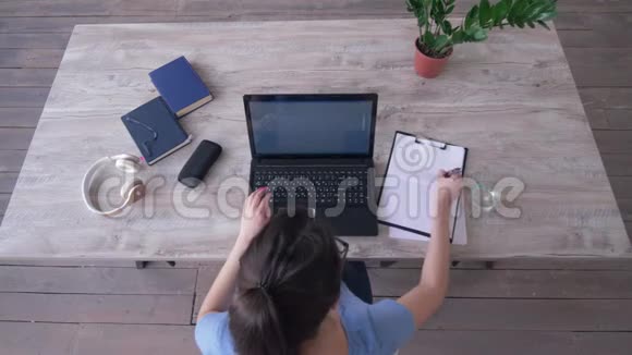 自由职业者女孩在剪贴板上画一个图形在工作时坐在桌上的笔记本电脑键盘上输入文字视频的预览图