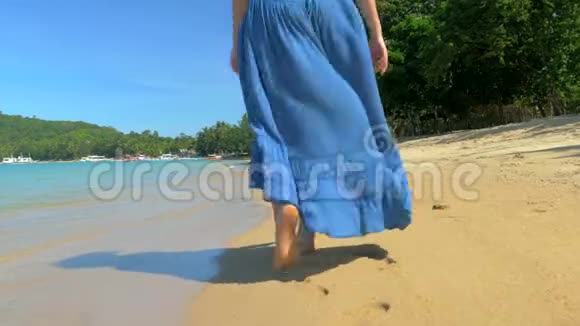 年轻的欧洲女孩穿着蓝色连衣裙在沙滩上漫步以大海和海浪为背景视频的预览图