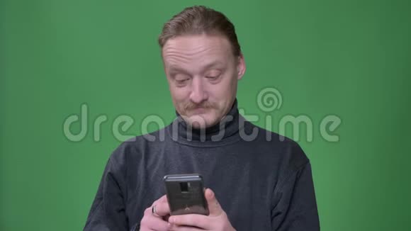 穿灰色套头衫的金发养老金领取者在绿色背景下对智能手机中的内容做出情感反应视频的预览图
