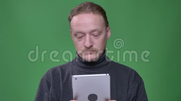 身着灰色套头衫的金发养老金领取者专心地看着平板电脑在绿色背景上赞许地点头视频的预览图