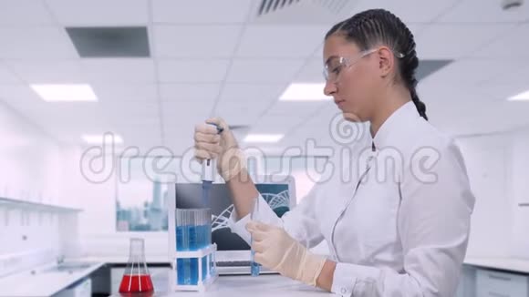一名女实验室技术人员在一张桌子旁坐着用微型吸管将蓝色液体样品转移到试管中视频的预览图